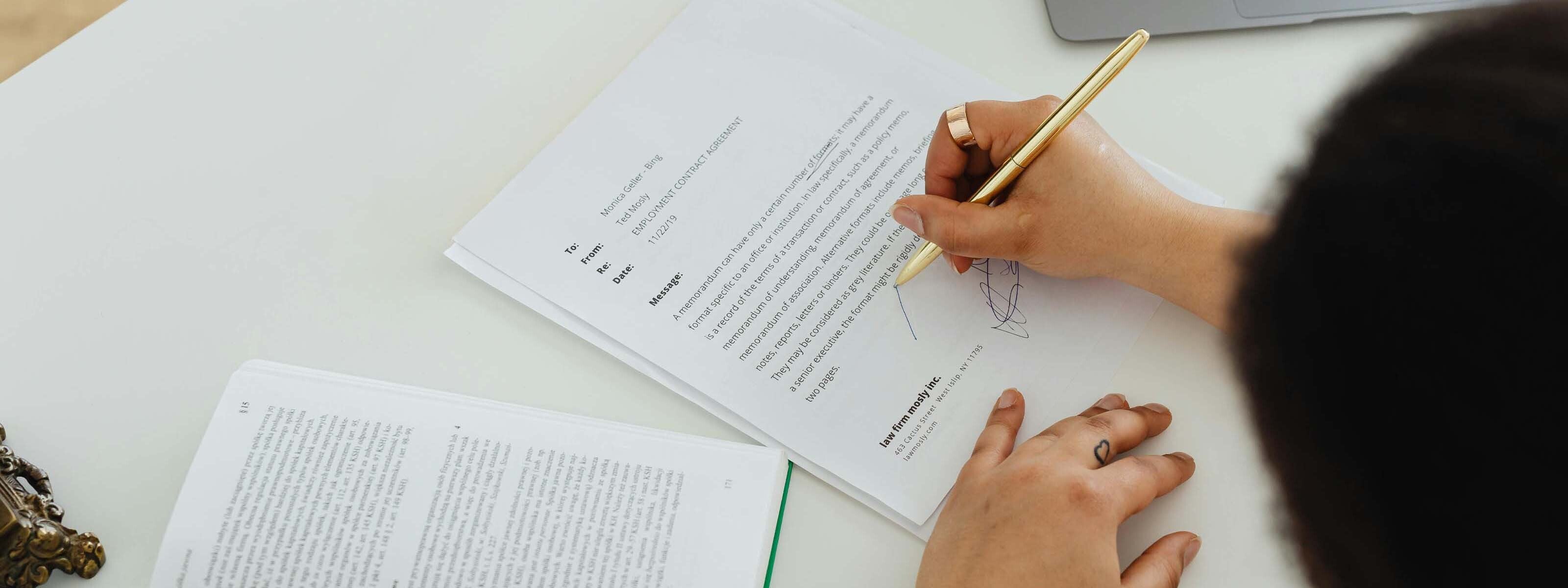 Persona firmando un documento con un bolígrafo dorado.