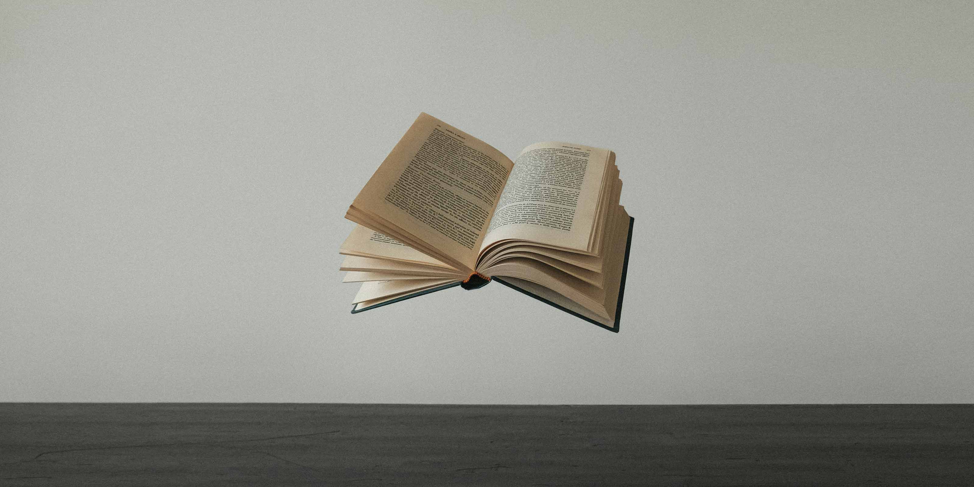 Un libro abierto flotando sobre una superficie gris.
